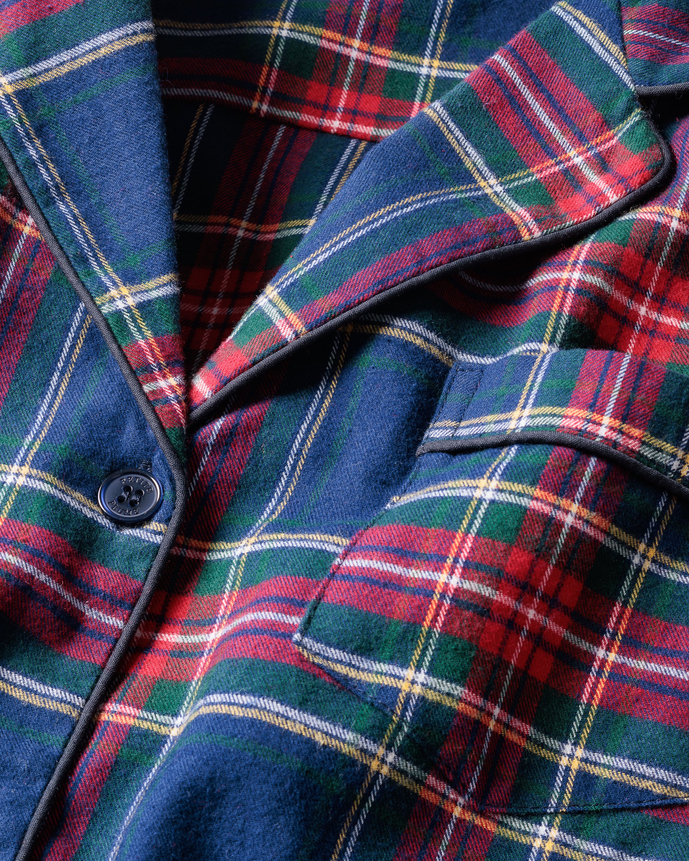 Close-up of a lavish Kids Brushed Cotton Pajama Set in Windsor Tartan by Petite Plume, showcasing red, blue, green, and yellow intersecting stripes forming squares and rectangles. A visible button and seam complete this classic pajama look.