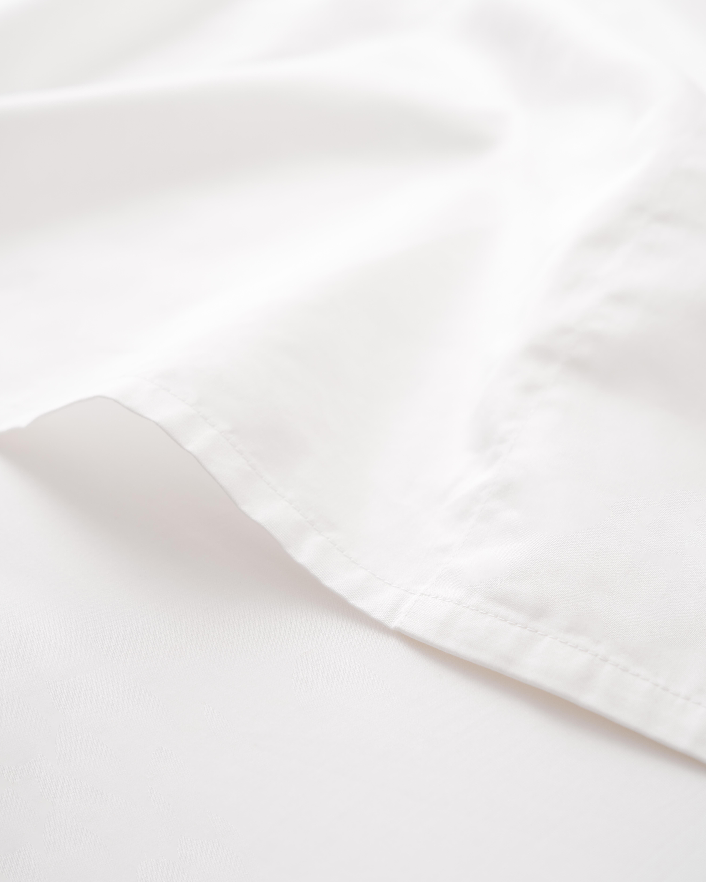 A close-up of the Signature Luxe Sateen Bed Sheets in White by Petite Plume reveals 100% long-staple cotton with a smooth texture and neat seams, luxuriously draped to form soft shadows and highlights like five-star hotel sheets.