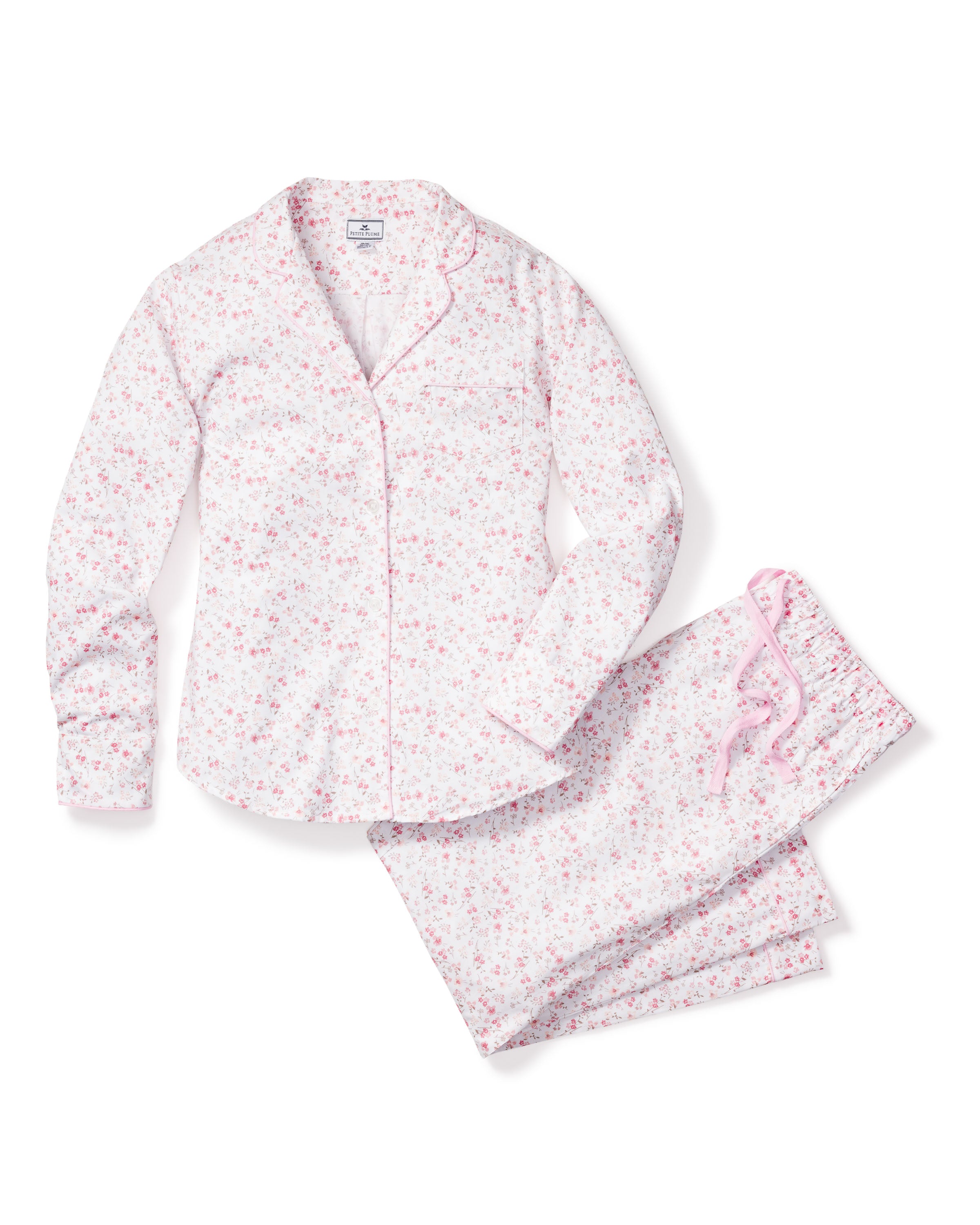 The Womens Twill Pajama Set in Dorset Floral by Petite Plume is crafted from the finest quality cotton, featuring a white design with a pink floral pattern. It includes a long-sleeve button-up top with pink piping and matching pants with a pink drawstring, embodying luxury and harmony.