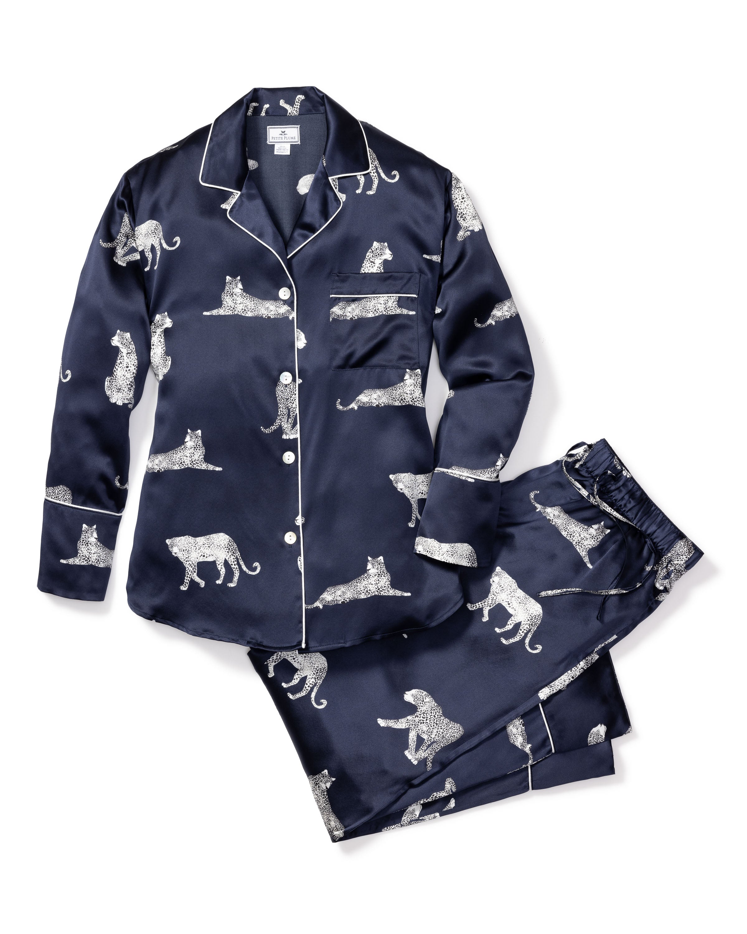 The Womens Silk Pajama Set in Panthère de Nuit by Petite Plume is navy blue with a Mulberry silk button-up shirt and pants. It features white jaguars in various poses and has white piping on the collar, cuffs, and pocket, offering elegant luxury sleepwear.