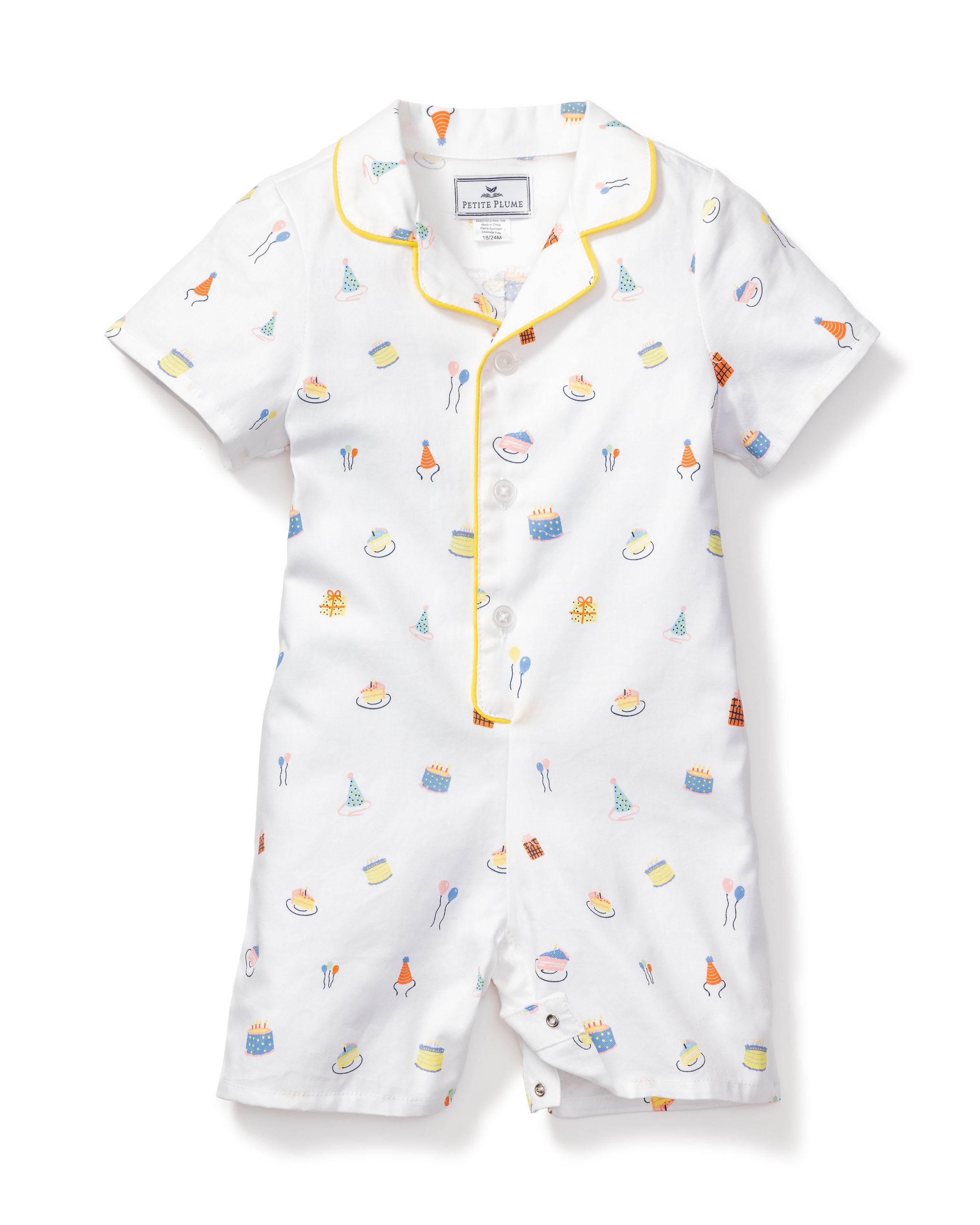 The Babys Twill Summer Romper in Birthday Wishes by Petite Plume is a white short-sleeve romper made from yarn-dyed cotton, featuring yellow piping and a playful birthday fantasy print with cakes and party decor. It has front button closures for easy dressing.