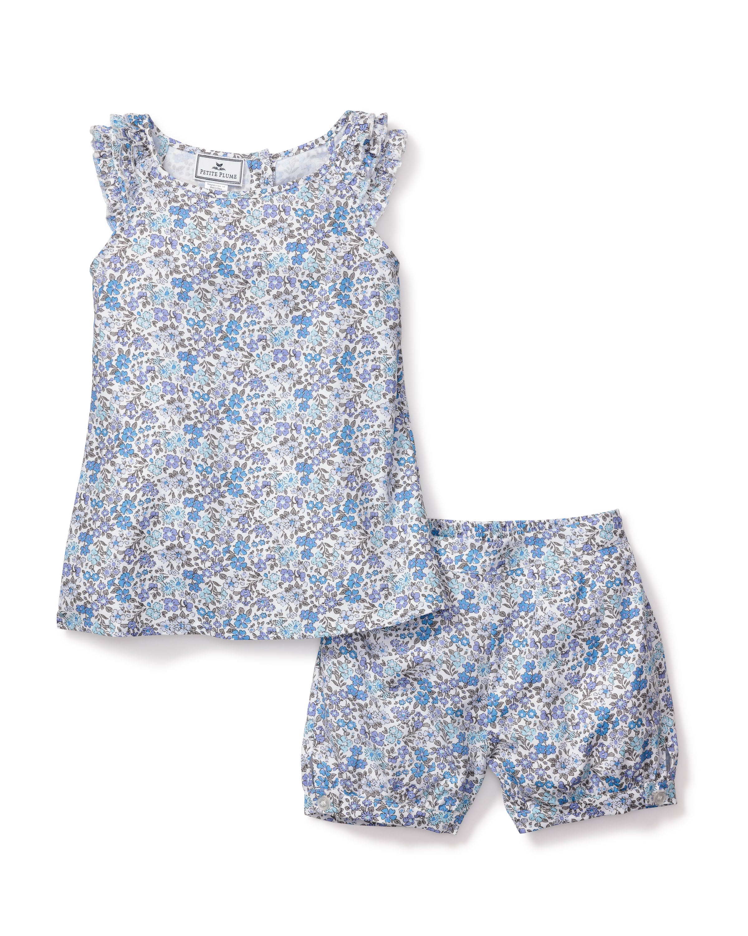 The Girls Twill Amelie Short Set in Fleur DAzur by Petite Plume is a luxurious sleepwear set. It includes a sleeveless top with ruffled shoulders and matching shorts with an elastic waistband. The blue floral pattern on white cotton offers comfort and vintage charm.