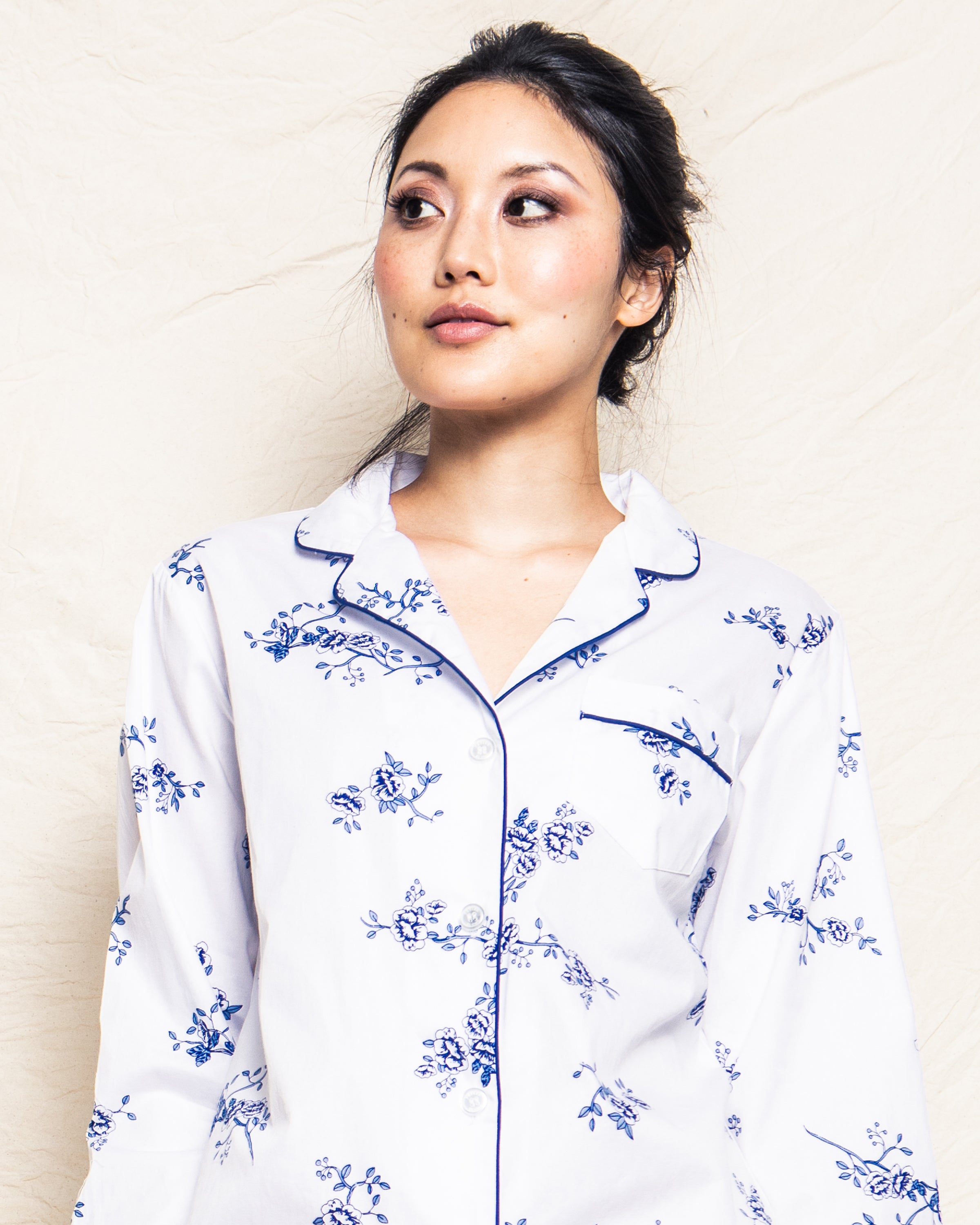 A person models the Womens Twill Pajama Set in Indigo Floral by Petite Plume, looking to the side against a light beige background.