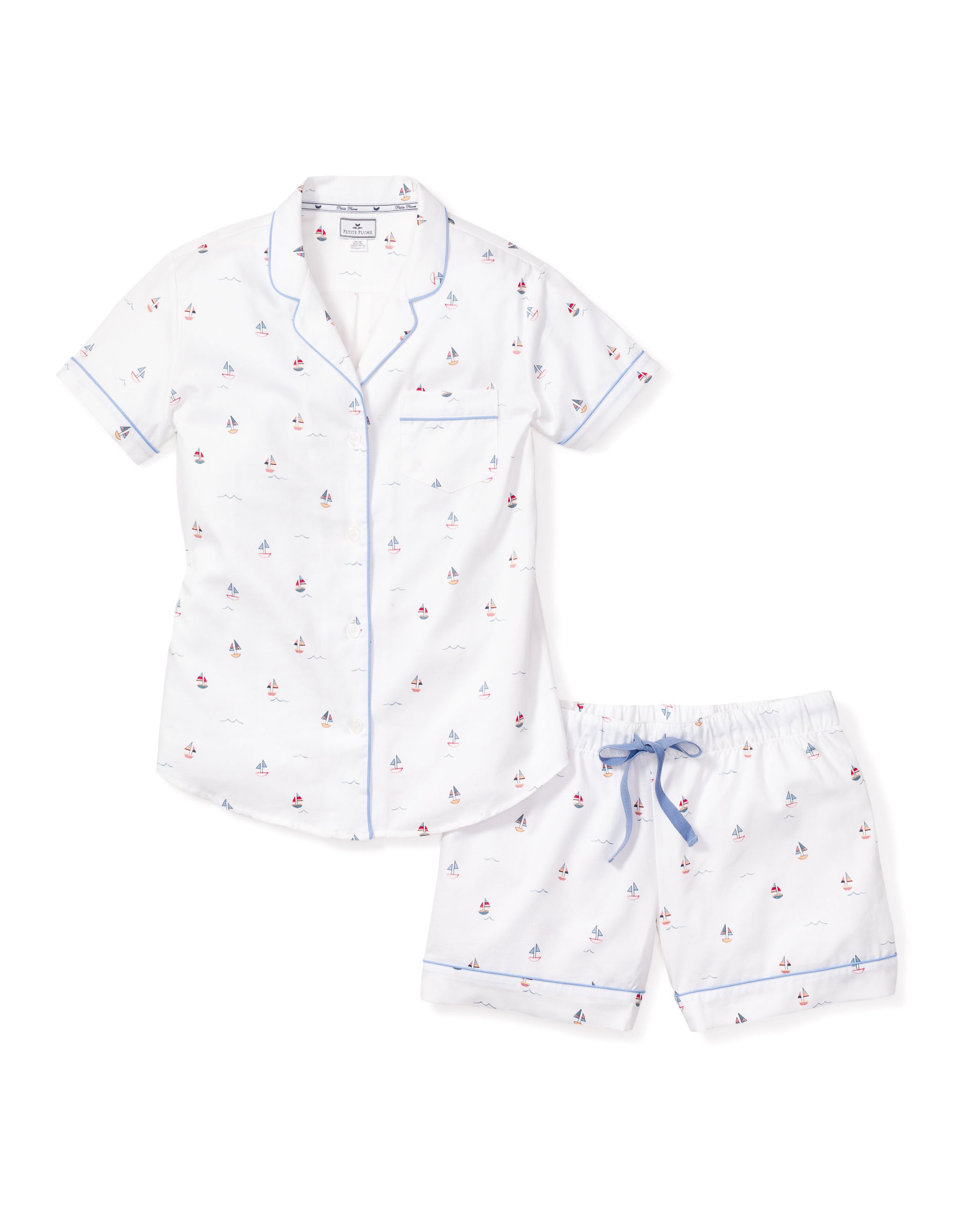 The Womens Twill Short Set in Bateau by Petite Plume features a white short-sleeved button-up top and shorts with blue trim and a small sailboat pattern. Designed for luxury, the set includes a chest pocket on the top and shorts with a stylish blue drawstring.