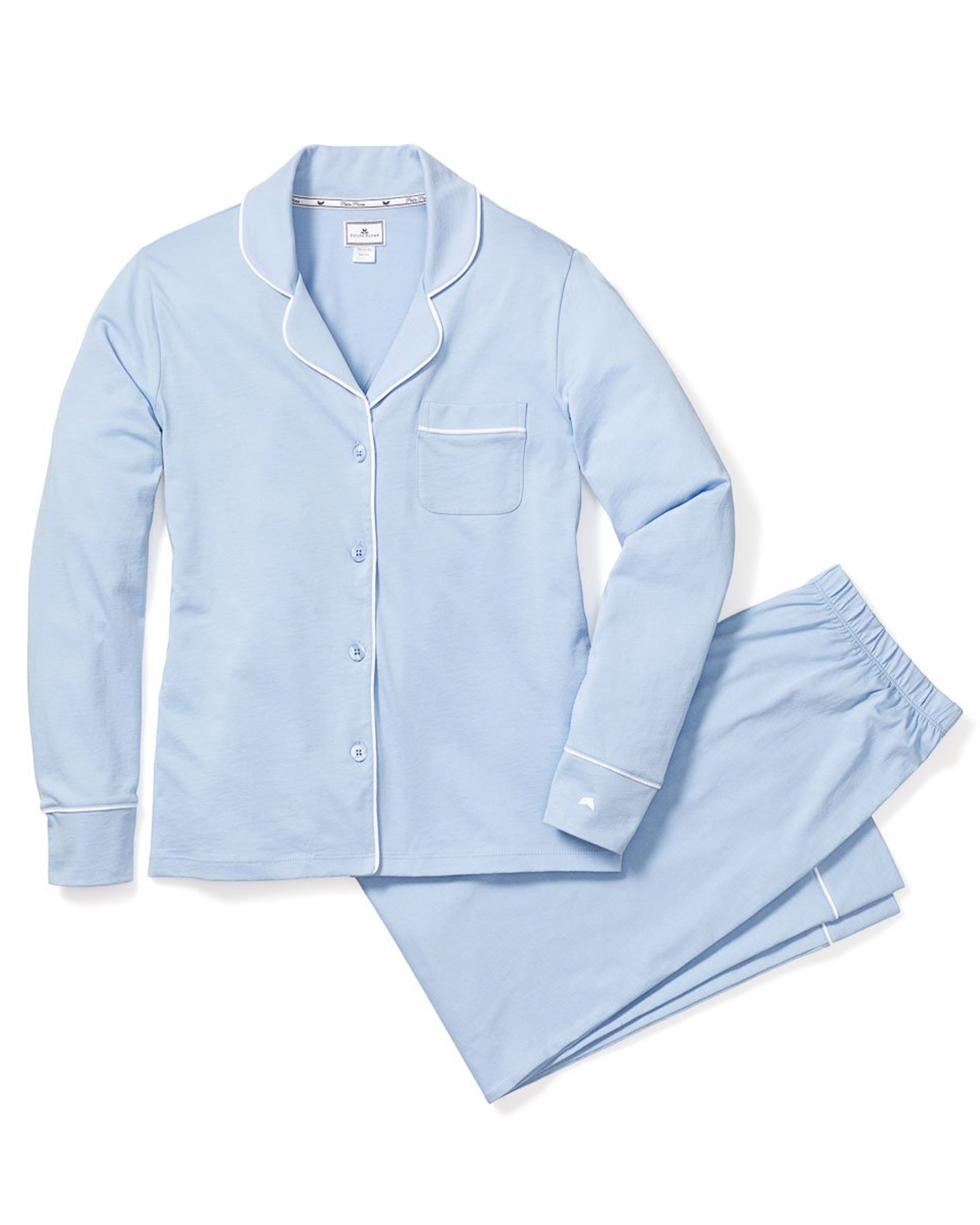 The Womens Pima Pajama Set in Periwinkle by Petite Plume features luxurious Peruvian Pima cotton. This light blue set includes a long-sleeve button-up top with a chest pocket and matching pants, enhanced by white trim and buttons for contrast, all displayed on a white background.