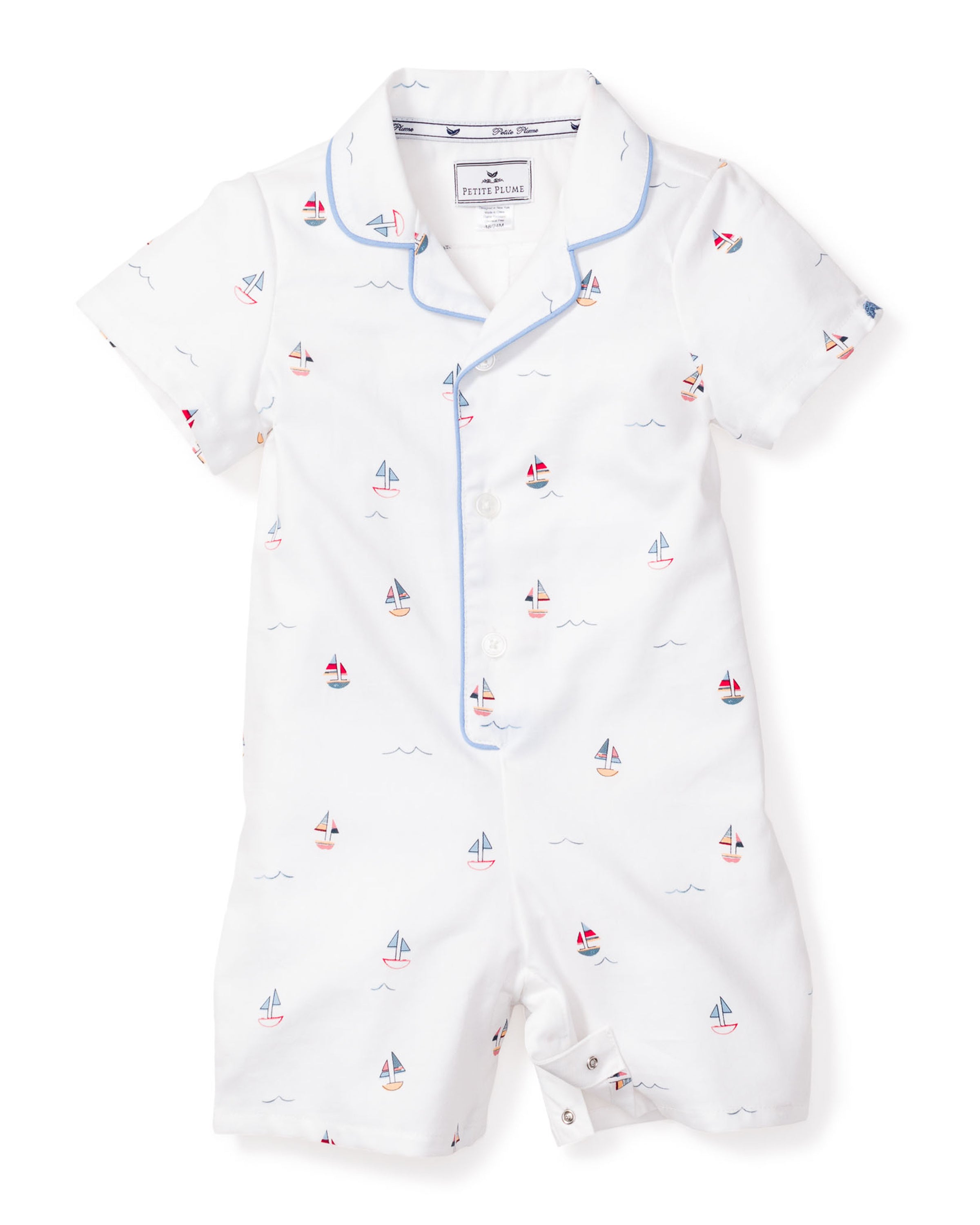 Petite Plumes Babys Twill Summer Romper in Bateau features a white base with a sailboat design in blue, red, and light brown. It includes a collared neckline with blue piping, short sleeves, and front buttons. Made from flame-retardant material, its ideal as sleepwear for safe and peaceful slumbers.