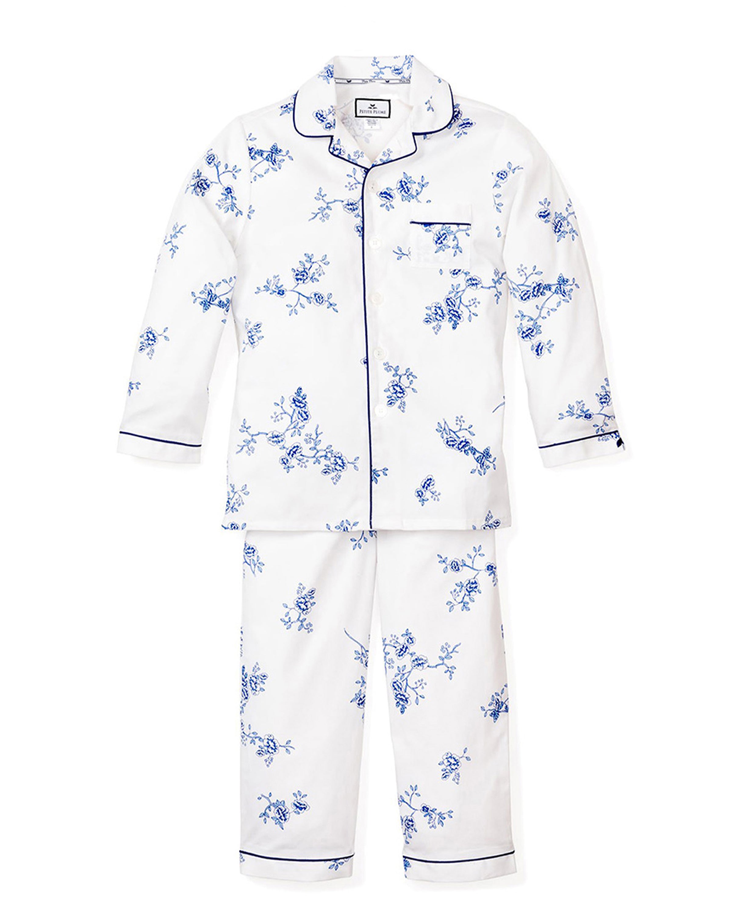 The Kids Twill Pajama Set in Indigo Floral by Petite Plume features a vintage-inspired white and blue floral design. The top has long sleeves, a collar, and a chest pocket with dark piping. The matching full-length pants complete this classic pajama set.